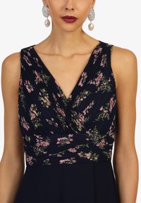 Marineblaues Kleid mit plissiertem Stoff und floralen Mustern in Rosa und Grün. V-Ausschnitt und taillierter Schnitt sorgen für eine schmeichelhafte Silhouette.