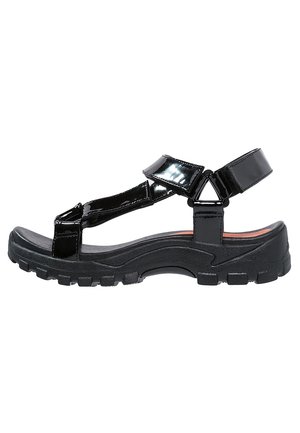 Sandalias de charol negro con una suela de goma gruesa y texturizada. Cuentan con múltiples correas ajustables y un diseño de punta redondeada.