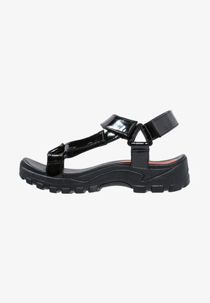 Czarne sandały z lakierowanej skóry z grubą, teksturowaną gumową podeszwą. Wiele regulowanych pasków i zaokrąglony przód buta.