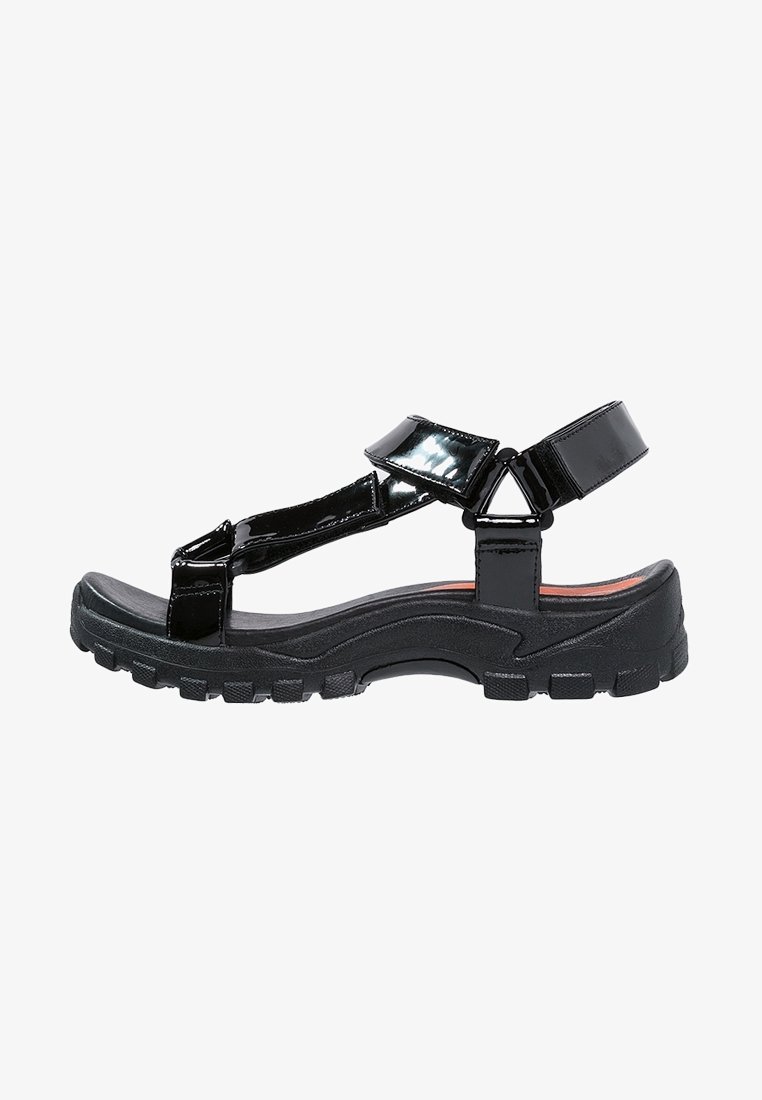 Sandales en cuir verni noir avec une semelle épaisse en caoutchouc texturé. Multiples brides ajustables et bout arrondi.