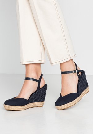 Marineblå espadrille kilehælssandaler med en flettet jute platform, justerbar ankrem og lukket tå design.