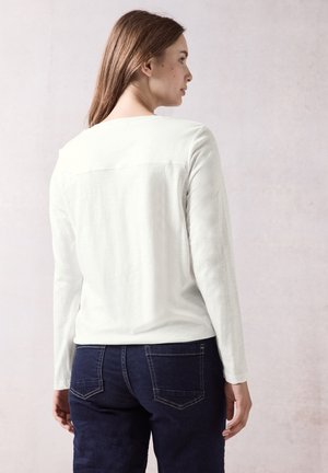 Wit langekatoenen top met ronde hals en stiksel, gecombineerd met donkerblauwe jeans met contrasterende stiksels en twee achterzakken.
