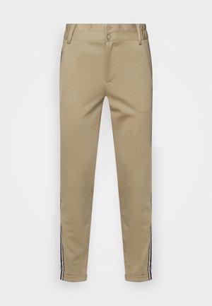 Pantalon beige fuselé avec revers retournés et bandes latérales noires et blanches, doté de passants de ceinture et d'une fermeture à double bouton.