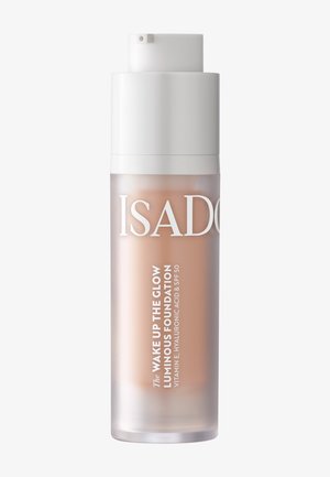 Klare mattierte Flasche der IsaDora Wake Up The Glow leuchtenden Foundation mit weißer Pumpkappe und sichtbarer hellbeiger Flüssigkeit darin.