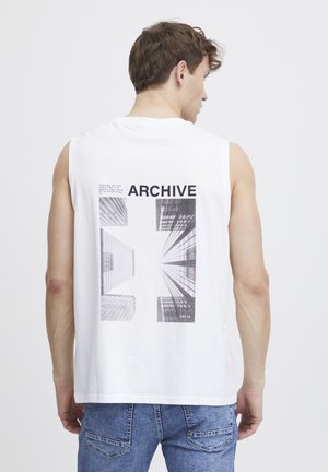 White sleeveless t-shirt featuring a graphic design of buildings on the back, with "ARCHIVE" text in bold black. Short hem and relaxed fit.