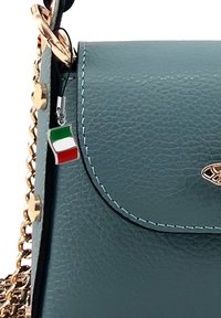 Teal leren handtas met gouden kettingband, met een gestructureerde afwerking, afgeronde klep en een kleine Italiaanse vlag charm eraan bevestigd.