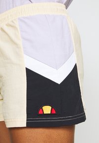 Kraťasy s barevnými panely ve světle fialové, krémové, bílé a černé barvě. Elastický pas s živým výšivkovým logem.