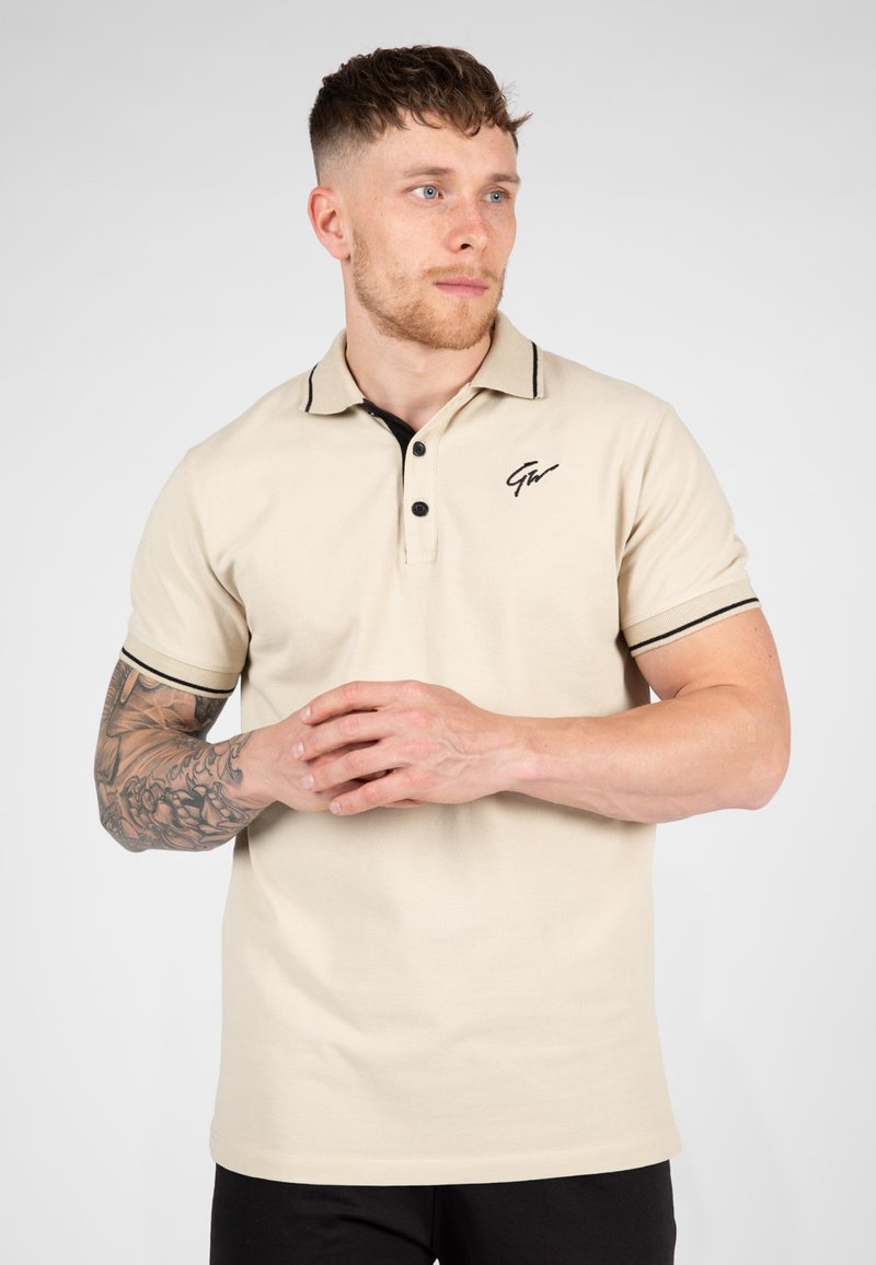 Beige poloshirt met zwarte kraagaccenten en zoom, voorzien van een drieknoopsluiting en een klein geborduurd logo op de borst.