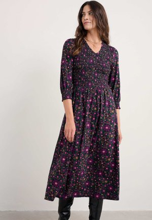 Lang, lilla kjole med et blomsterprint i pink og grøn. Har smock-detaljer ved bodicen og ærmer i tre kvarte længde. Glat stof.