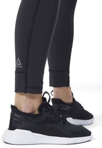 Czarne legginsy sportowe o eleganckim fasonie, w połączeniu z lekkimi czarnymi adidaskami z siateczkowymi akcentami i białą podeszwą.