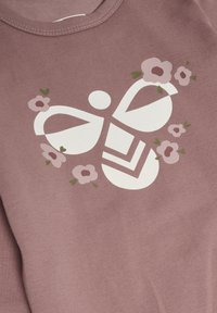 Rosa bomullsskjorta med en stor vit bi-grafik omgiven av rosa och gröna blomster mönster. Mjuk struktur och rund halsringning.