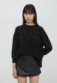 Czarny sweter o fakturowanym splocie, z białymi ozdobami w postaci perełek rozsianych na przodzie, połączony z czarnymi szortami z ekoskóry.