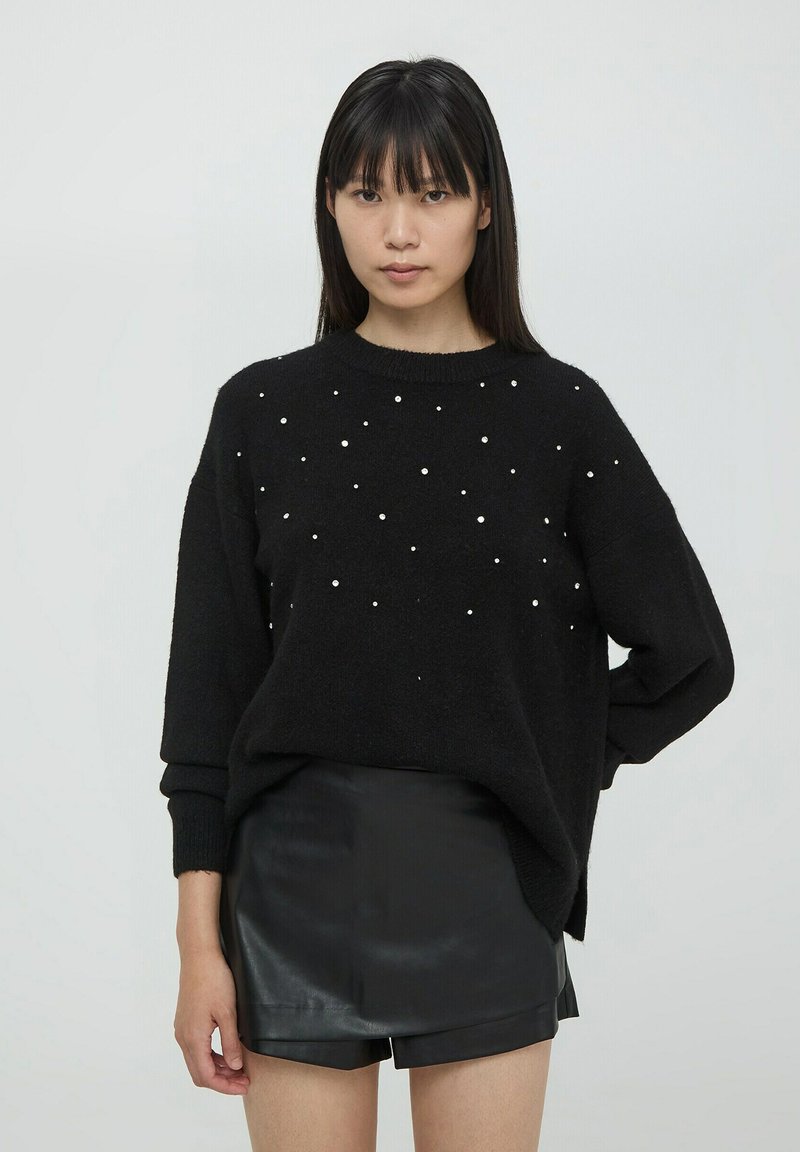 Czarny sweter o fakturowanym splocie, z białymi ozdobami w postaci perełek rozsianych na przodzie, połączony z czarnymi szortami z ekoskóry.