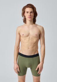 Boxers en olive pour homme avec une taille élastique noire, texture lisse et design ajusté, affichés sur un mannequin torse nu.