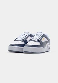 Hvide og marineblå sneakers med glat læder og perforeret tå. Har hvide snørebånd og en grå sål. PUMA-logoet er vist på siden.