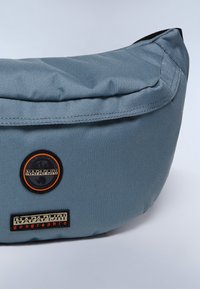 Borsa in tessuto blu con superficie texturizzata. Presenta un logo circolare e un'etichetta rettangolare, entrambi con colori a contrasto.