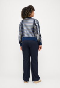 Stripet marineblå og beige genser med ribbede ermer, kombinert med marineblå vide bukser og beige sneakers. Teksturert stoff, avslappet passform.