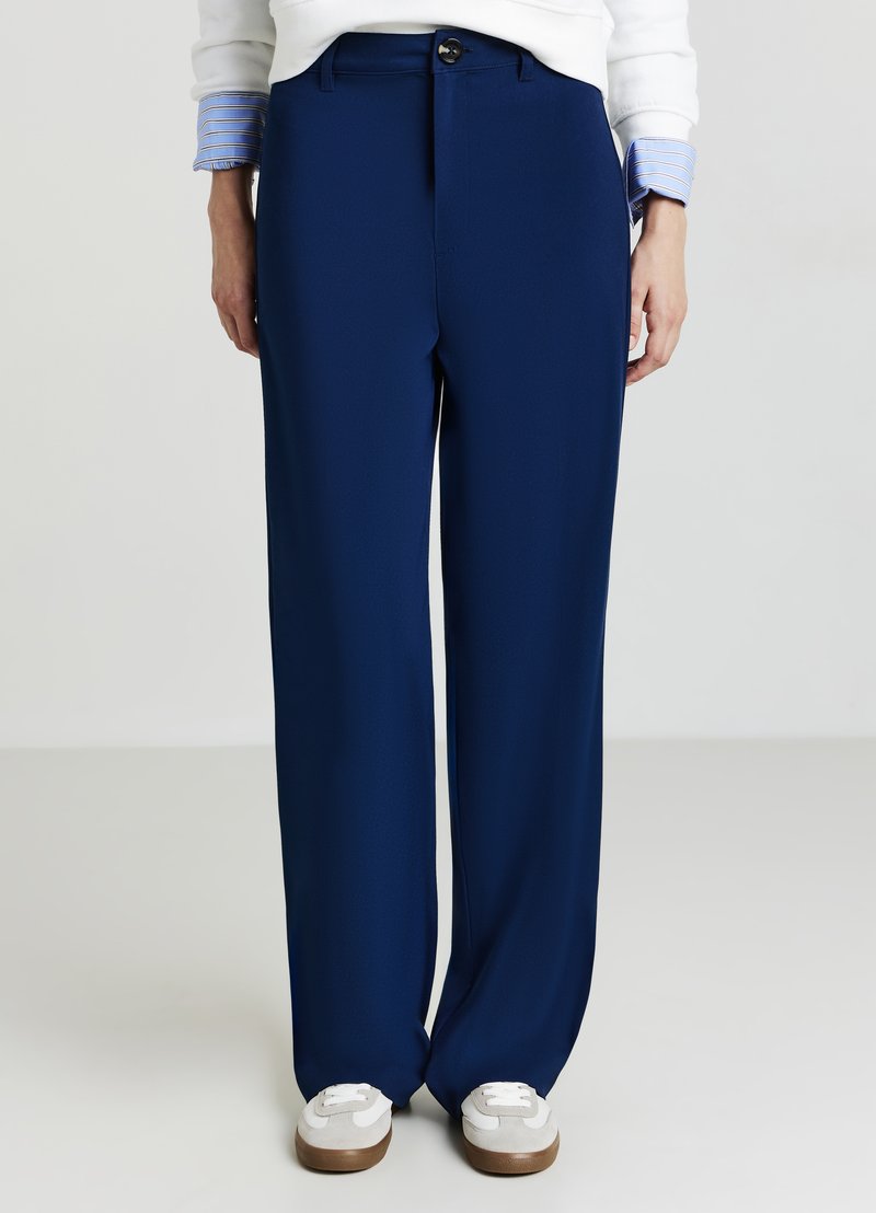 Marineblaue weite Hose aus glattem Stoff mit normaler Taille und vorderem Knopfverschluss, kombiniert mit weißen Sneakers.