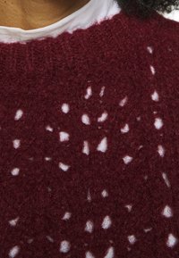 Maglione in borgogna lavorato a maglia con un motivo a rete aperta, caratterizzato da piccoli ritagli, superficie testurizzata e collo a coste.