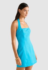 O rochie fără mâneci, cu decolteu pătrat, în culoarea turcoaz strălucitor, având un corset ajustat și o fustă evazată, confecționată dintr-un material neted cu cusături minime.