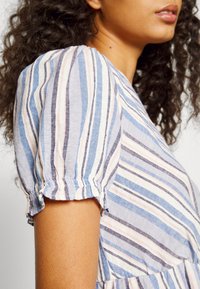 Robe à manches bouffantes en tissu léger avec des rayures verticales bleu, rose et blanc. Elle présente des poignets élastiqués et une silhouette décontractée.