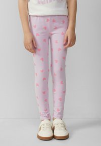 Lichtroze leggings met een herhaald aardbeienpatroon in roze met groene accenten, gecombineerd met crèmekleurige sneakers.