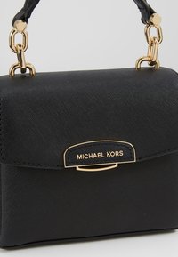 Zwarte leren handtas met een gestructureerd oppervlak, gouden accenten en een voorvaksluiting met de merknaam "Michael Kors." Klein en compact ontwerp.