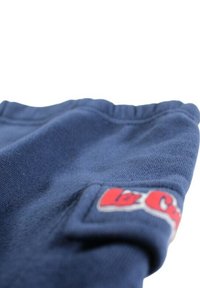 Tissu de sweat-shirt bleu marine avec une texture côtelée et un ourlet élastique. Présente un patch logo rouge et blanc sur le côté inférieur gauche.