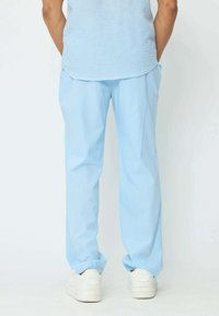 Pantalons baggy bleu clair en tissu lisse, avec un design simple et des ourlets roulés, associés à des baskets blanches.