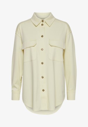Světle žlutá košile na knoflíky s límečkem, která má dvě náprsní kapsy, zaoblený spodní lem a dlouhé rukávy s manžetovými knoflíčky.