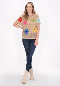 Krémový pletený top s barevnými květinovými aplikacemi v červené, růžové, modré, zelené a světle modré; spárováno s tmavými skinny džíny a krémovými kotníkovými botami.