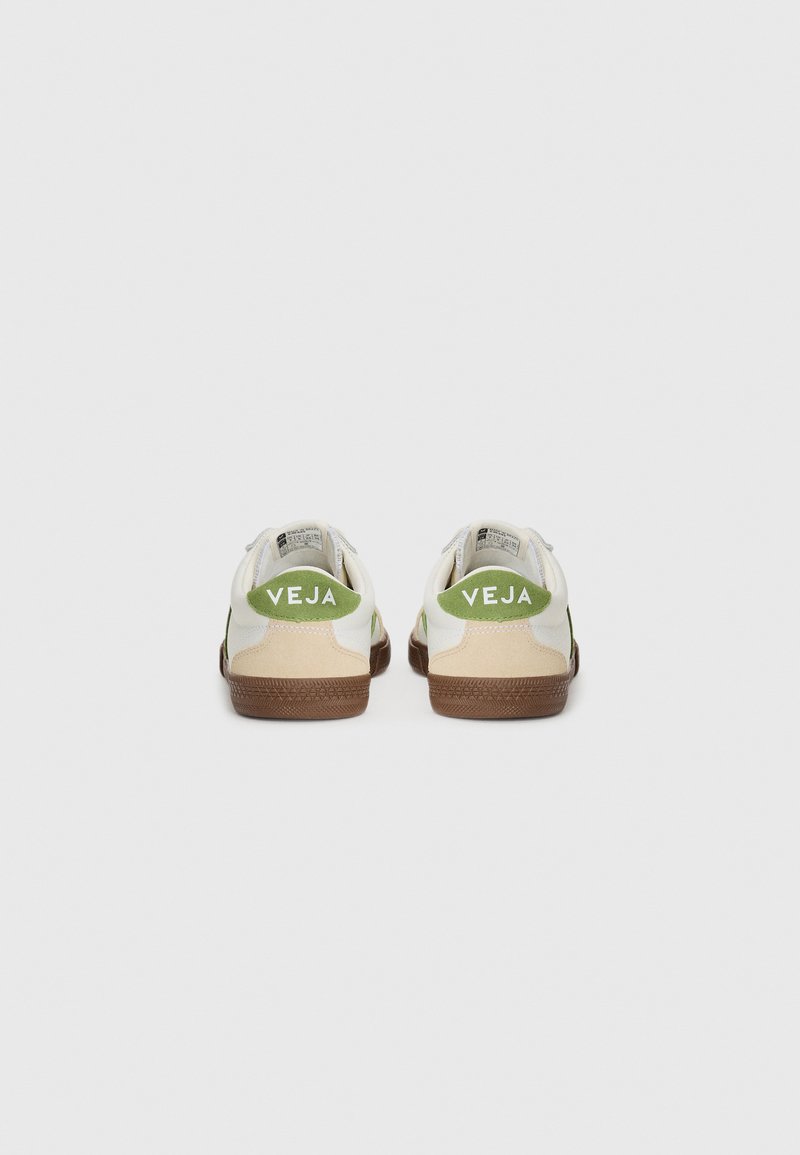 Baskets en cuir blanc avec des accents verts et beiges, dotées d'une semelle en caoutchouc marron texturée et du logo "VEJA" au niveau du talon.