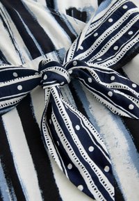 Kék-fehér anyag függőleges csíkokkal és egy nagy masnival. A masnin pöttyök és finom vonalminták találhatók. Puha textúra.