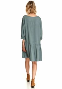 Vapaa, puolipitkä mekko muted teal -värisessä kankaassa, jossa on kolme neljännesosapituista hihoista ja kerroksellinenhelma. Mekoissa on pyöreä pääntie ja nappikoristeet.
