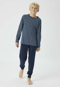Navy and white striped long-sleeve shirt paired with solid navy pants, both made of soft fabric. Model stands barefoot, smiling.