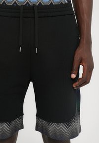 Mustad mustad lühikesed püksid elastse vöökoha ja halli ja sinise tooni sakilise äärisega. Valmistatud pehmest ja venivast kangast.