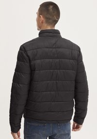 Jachetă puf din material negru, cu guler înalt, design cu cusături orizontale, textură netedă și manșete elastice. Fabricată dintr-un material ușor, rezistent la apă.