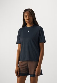 T-shirt à manches courtes bleu marine foncé avec un col rond et un petit logo blanc au centre. Le mat�ériau semble doux et léger.