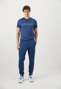 Plava pamučna majica s natpisom "BJÖRN BORG" i odgovarajuće plave trenirka hlače, s mekom teksturom i elastičnim pojasom, uparene s bijelim tenisicama.