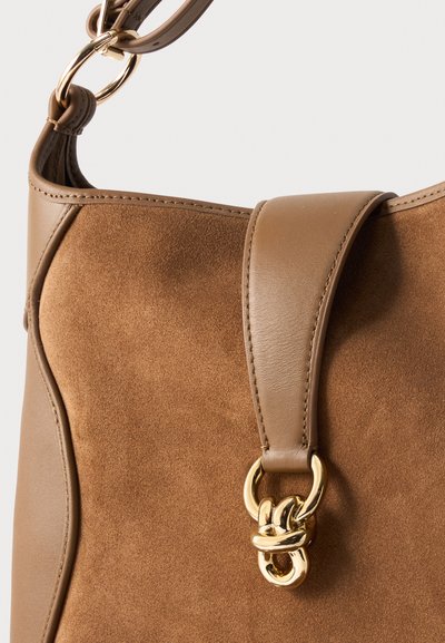 Καφέ τσάντα από σουέντ και δέρμα με χρυσό μεταλλικό κούμπωμα και ρυθμιζόμενο λουρί ώμου σε λευκό φόντο.