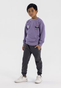 Felpa viola con dettagli grafici, pantaloni della tuta grigi e sneakers bianche. La felpa presenta un colletto rotondo e maniche con polsini.