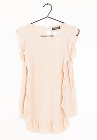 Blusa senza maniche di un rosa chiaro con bordi arricciati sui lati e sul fondo, appesa a una gruccia nera su uno sfondo bianco.