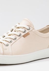 Light beige leather sneaker featuring white laces, silver eyelets, and a cream rubber sole. Includes a small tan ECCO logo accent.