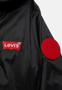 Giacca nera con logo Levi's ricamato rosso e una toppa rossa con design montano sulla manica. Tessuto dalla superficie liscia.