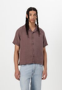 Brun ternet kortærmet skjortebluse med blødt, struktureret stof. Skjorten har en afslappet pasform og en diskret krave, båret med lyse jeans.