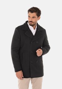 Cappotto di lana nero con design doppiopetto, ampio colletto e due tasche laterali. Presenta bottoni rotondi neri e una texture liscia.