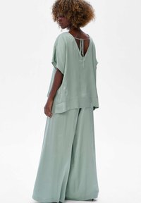 Jasnozielony, satynowy dwuczęściowy zestaw, obejmujący luźną bluzkę z szerokimi rękawami i głębokim dekoltem na plecach, zestawiony z szerokimi spodniami.