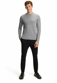Graues Langarmshirt mit rundem Ausschnitt, kombiniert mit schwarzen schmal geschnittenen Hosen und schwarzen Turnschuhen. Glatte Textur, figurbetontes Design.