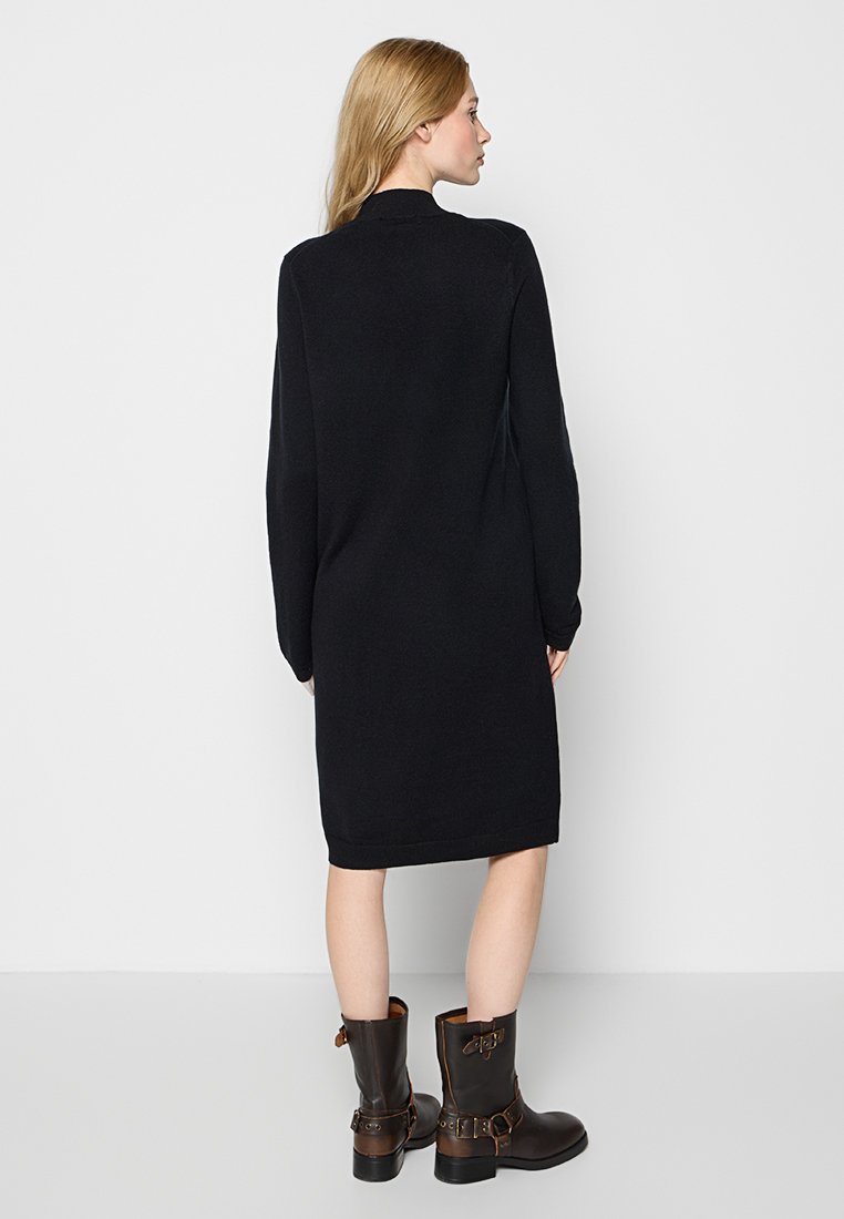 Czarna sukienka z długim rękawem, do kolan, z miękkiego materiału, o swobodnym kroju. Połączona z brązowymi botkami do kostki z klamrami i paskami.