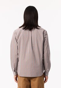 Camisa de manga larga de cuadros marrones y blancos con cuello abotonado y pliegue en la espalda, hecha de una tela ligera.